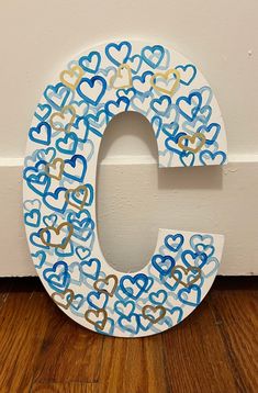 the letter c is painted with hearts and gold paint on it's side, next to a white wall