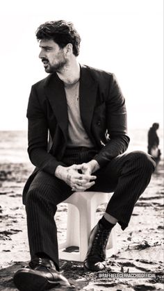 a man sitting on top of a white toilet in the sand next to the ocean