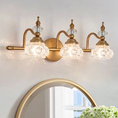 a bathroom vanity light with three lights and a mirror on the wall next to it