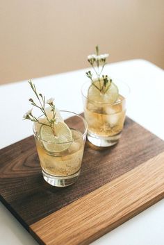 two glasses filled with drinks sitting on top of a wooden cutting board