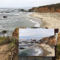 an easel with a painting on it next to the beach and ocean in the background