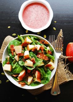 a salad with apples, bacon and spinach in a bowl next to a fork