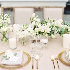 the table is set with white flowers and greenery in glass vases on gold rimmed plates