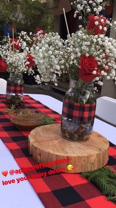 three vases with flowers are sitting on a wooden slice at a table that has red and black checkered cloth