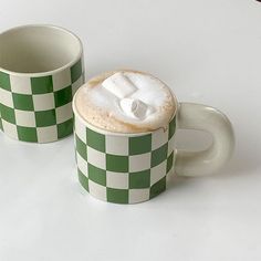 two green and white checkered coffee mugs with foamy toppings on them