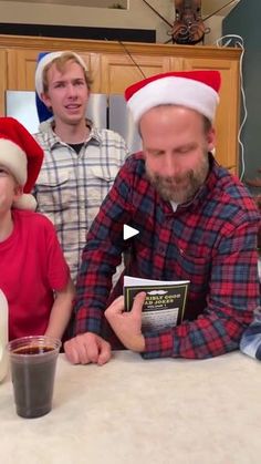 a man sitting at a table with two children wearing christmas hats and reading a book