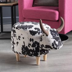 a cow shaped ottoman sitting on top of a hard wood floor next to a pink chair