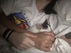 a person laying in bed with a cat on top of their stomach and holding it