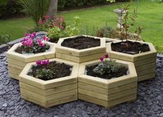 a group of wooden planters sitting on top of a gravel covered ground next to flowers