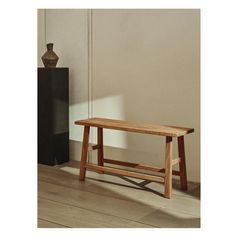 a wooden bench sitting on top of a hard wood floor next to a tall vase