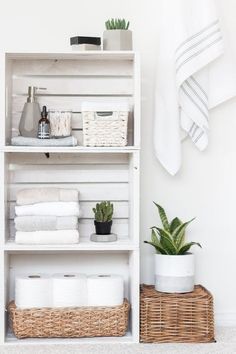 a white shelf filled with lots of towels next to a basket and potted plant