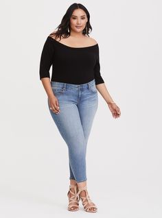 a woman standing in front of a white background wearing blue jeans and a black top