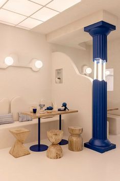 a room with white walls and blue columns on the floor, along with stools and tables