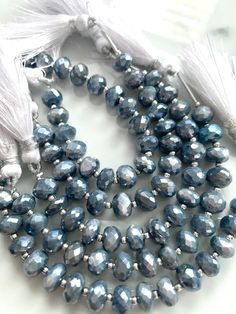 two strands of gray glass beads with tassels on white table top next to other beads