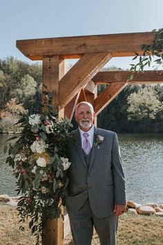 a man in a suit standing next to a wooden structure with flowers and greenery