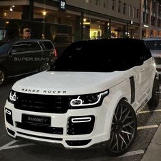 a white range rover parked on the side of a road next to other cars in front of a building