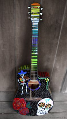 an acoustic guitar decorated with sugar skulls and day of the dead decorations is displayed in front of a wooden wall