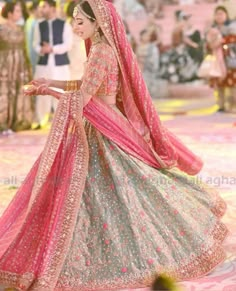 a woman in a pink and green lehenga is walking down the runway with her hand on her hip