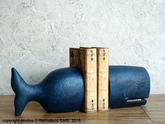 a blue whale shaped bookend sitting on top of a wooden table next to a white wall