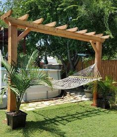 an outdoor hammock in the middle of a yard with a tree and potted plant