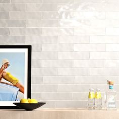 a framed photograph sitting on top of a table next to lemons and bottles in front of a white brick wall