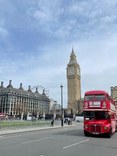 a red double decker bus driving down a street next to tall buildings and a clock tower