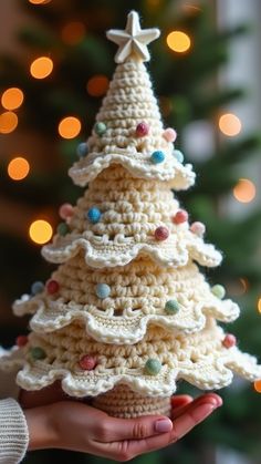 a crocheted christmas tree is being held in front of a decorated christmas tree