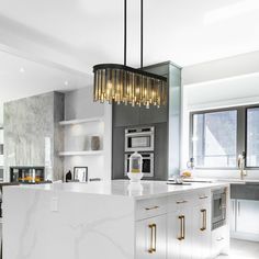 a modern kitchen with marble counter tops and gold accents on the pendant lights over the island