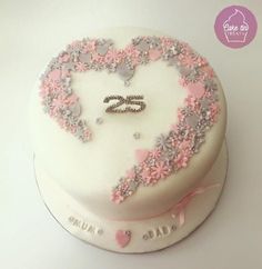 a white cake with pink and silver decorations on it's side, in the shape of a heart