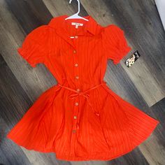 This Is A Flowy Dress That Is Fitted Around The Waist, And Has Ruffled Edges Around The Sleeves. The Wooden Buttons Go Perfect With This Color Orange And It Brings The Look Together. 100% Polyester And Made In India Trendy Short Sleeve Shirt Dress For Beach, Trendy Short Sleeve Shirt Dress For The Beach, Collared Vacation Dress With Buttons, Collared Dress With Buttons For Vacation, Collared Button Dress For Vacation, Fitted Shirt Dress With Buttons For Vacation, Summer Knee-length Buttoned Shirt Dress, Summer Knee-length Shirt Dress With Buttons, Red Button-up Vacation Dress