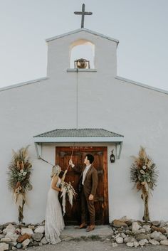 a bride and groom standing in front of a church door with their wedding bouquets