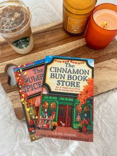 the cinnamon bun book store sits on a tray next to two cups of tea and a candle