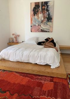 a woman laying on top of a white bed in a bedroom next to a painting