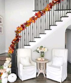 two white chairs sitting next to each other in front of a stair case with fall leaves on it