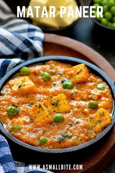 a pan filled with food on top of a wooden plate next to peas and potatoes