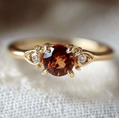 a gold ring with an orange stone and two diamonds on the side, sitting on top of a white cloth