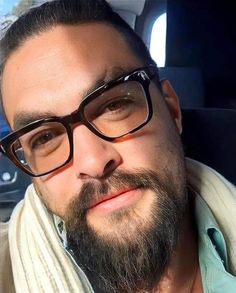 a man with glasses and a beard wearing a scarf in the back seat of a car