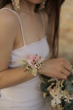 a woman in a white dress holding a bouquet of flowers and greenery with her hands