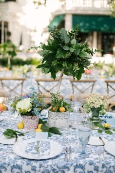 a table set up with plates and vases filled with flowers, fruit and greenery