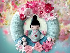 a crocheted doll sitting in front of a wreath with pink and white flowers