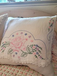 a white pillow with flowers on it sitting on top of a bed next to a window