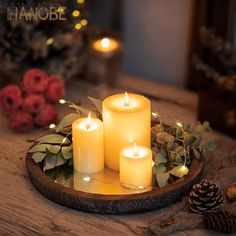 three lit candles sitting on top of a wooden tray with greenery and pine cones