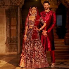 two people standing next to each other wearing red outfits and gold jewelry on their wedding day