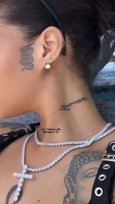 a woman with tattoos on her back and neck is wearing a black shirt, silver bracelets and a cross necklace