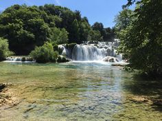 the water is crystal green and there are many waterfalls in the background with trees on either side