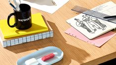 a wooden table topped with lots of office supplies next to a cup of coffee and scissors