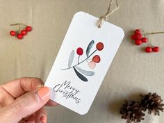 a hand holding a merry christmas tag with berries on it