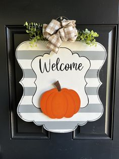 a welcome sign hanging on the front door with a pumpkin and greenery around it