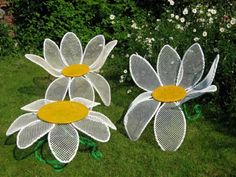 three metal flowers sitting on top of green grass next to white and yellow daisies