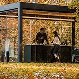 two people sitting at a table in front of a glass structure with trees and leaves around it